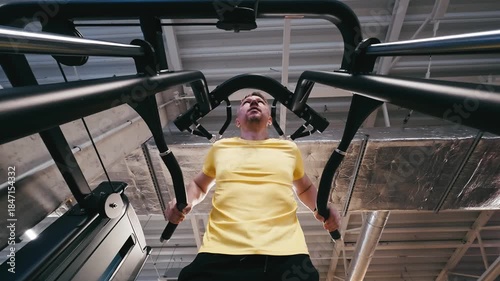 Man Performs Assisted Dips On Parallel Bars In The Gym With Legs Supported, Viewed From Below