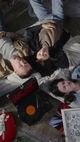 Vertical top view shot of group of friends lying on floor in circle and listening to music with old record player while chilling together in unoccupied building