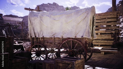 A rustic wooden wagon, covered with a white cloth, is positioned among crates in an outdoor setting. The background features rocky cliffs and scattered vegetation, indicating a remote location.