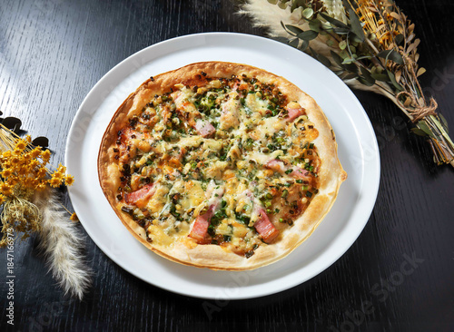 Delicious homemade pizza on white plate with fresh herbs and flowers