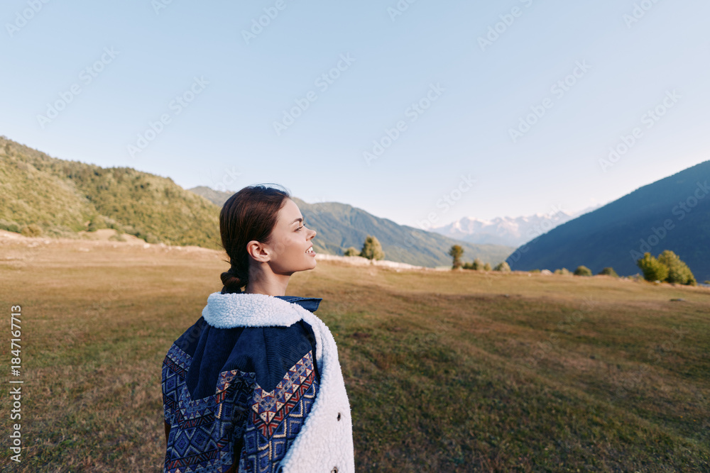 Naklejka premium Woman portrait with backpack in mountain landscape and wide meadow, hiking and travel scene at sunrise. Young traveler enjoying nature, panoramic view and outdoor exploration.