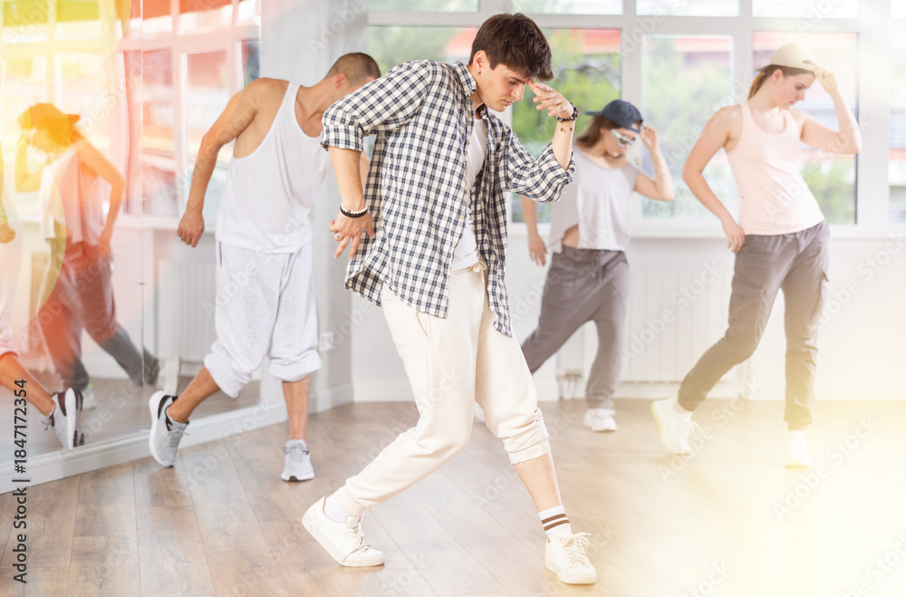 Fototapeta premium Positive young man engaged in hip-hop together with other attendees of dancing courses
