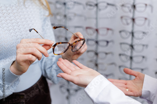 Hands passing eyeglass frames during optician consultation in optical store eyewear selection