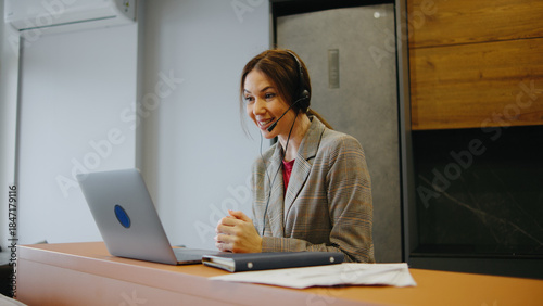 Woman at a desk using a laptop and headset while talking to a client in an office setting during daytime
