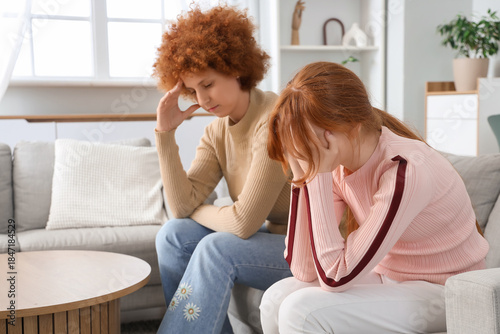 Upset mother with her teenage daughter sitting on sofa after squabble at home