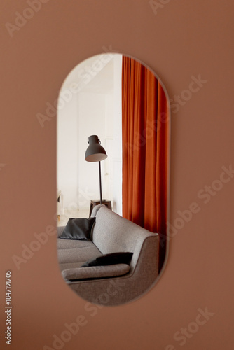 Oval mirror on a terracotta wall reflecting a modern living room with a sofa and floor lamp