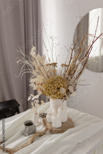Dried flower arrangement in a white vase with candles on a draped fabric surface