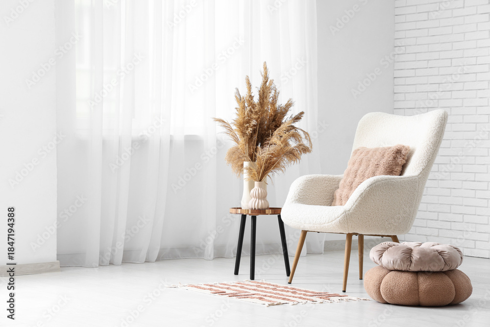 Naklejka premium Interior of light living room with armchair, table and pampas grass in vases