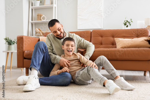 Tableau sur toile Happy father having fun with his son on floor near brown leather sofa at home