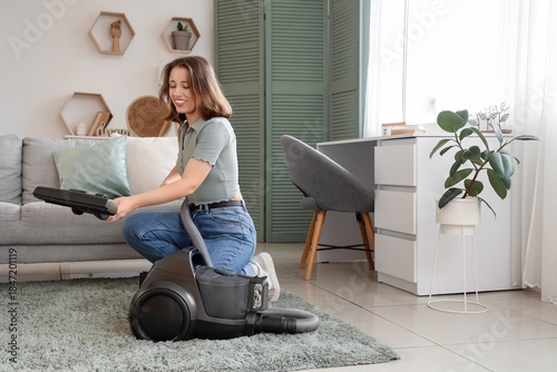 Young woman with vacuum cleaner on carpet in living room