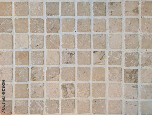 Natural stone mosaic tile texture. Square tesserae in beige, cream and brown with veining and light-colored grout. Small marble slab cladding for interior wall, bathroom, kitchen, patio, pool. 