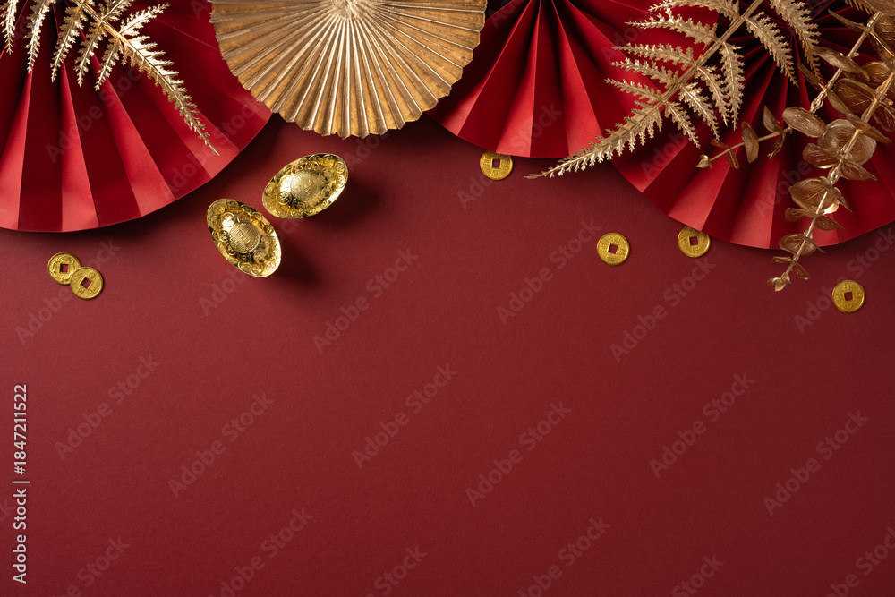 Fototapeta premium Vibrant red backdrop with gold coins, paper fans, and dried foliage captures the festive mood of Chinese New Year greetings and celebration with a luxurious, auspicious feel