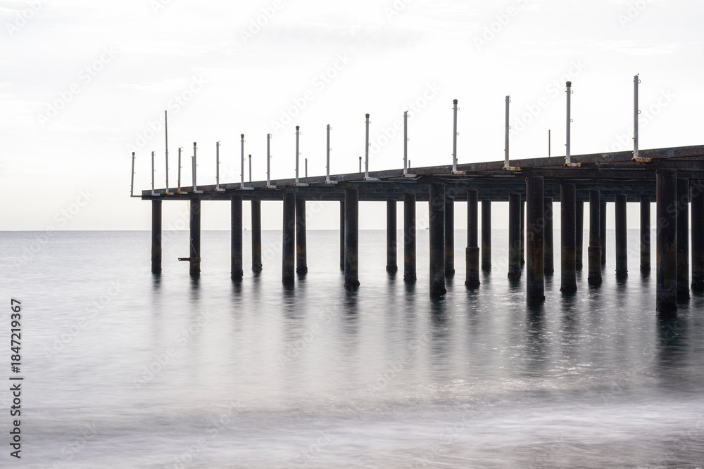 Obraz premium Old Pier Standing Over Calm Sea Water. Abandoned Pier Over the Sea. Deserted Wooden Pier in Seascape. Lonely Abandoned Dock Extending into the Ocean.