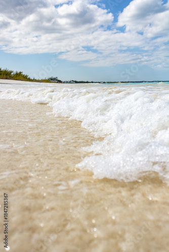 Sunny Beach With White Foam Waves Lapping The Clear Shore Under A Bright Sky