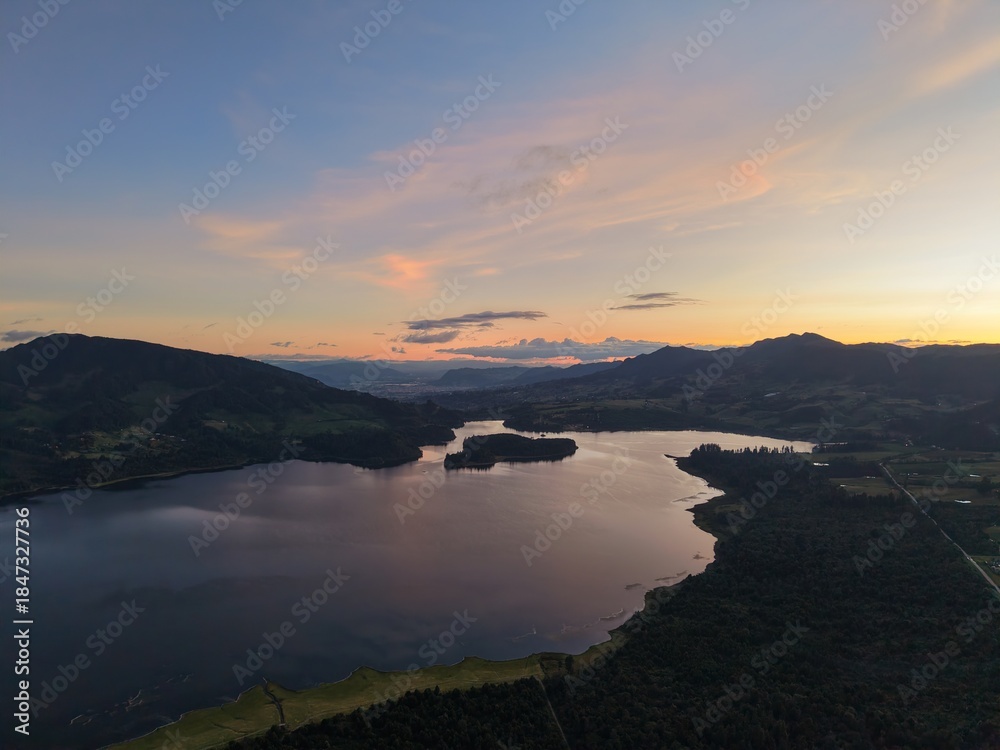 Obraz premium Vista aérea de la Represa del Neusa, Cundinamarca, con bosque y reflejos en el agua al atardecer.