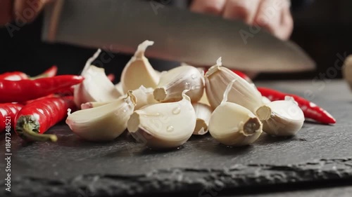 Gently gliding dolly shot across vibrant whole red chili peppers and fragmented white garlic cloves resting on a dark slate cutting board ready for meal preparation cutting board, vegetable, tabletop