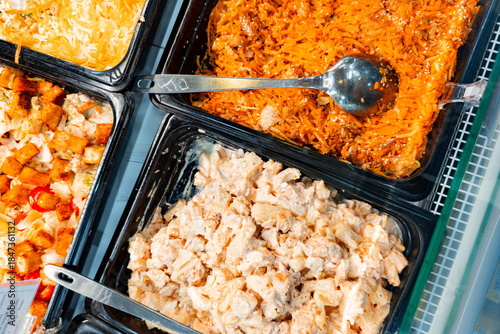 Variety of food containers with chicken, noodles, and shredded cheese displayed in a food setting during lunch time