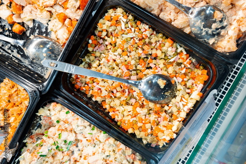 Fresh deli salads and prepared foods displayed in black containers on a shelf in a grocery store during the daytime