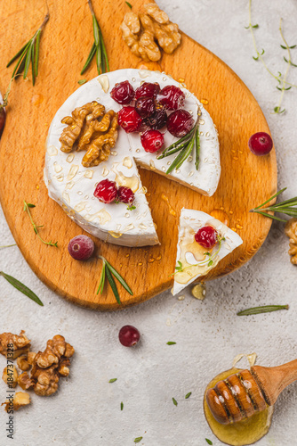 Brie cheese on a board with walnuts, honey and berries
