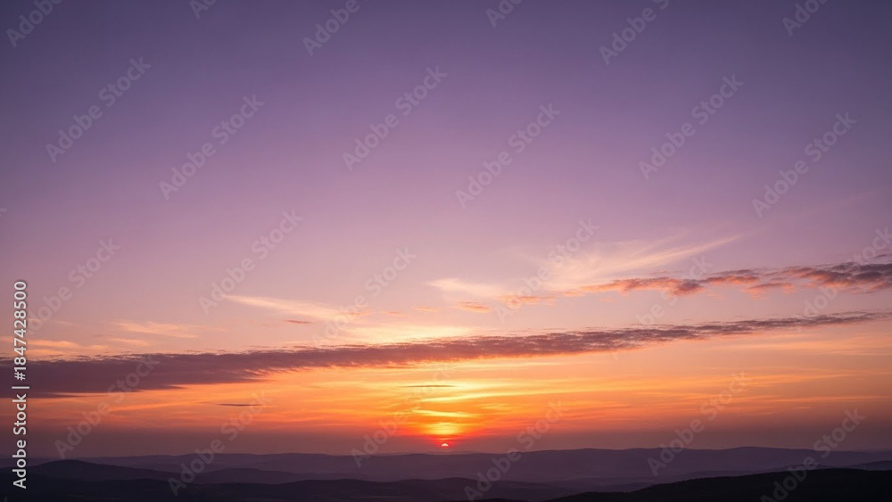 Fototapeta premium Dramatic sunset with vibrant orange and yellow hues illuminating the sky over distant rolling hills Keywords: sunset