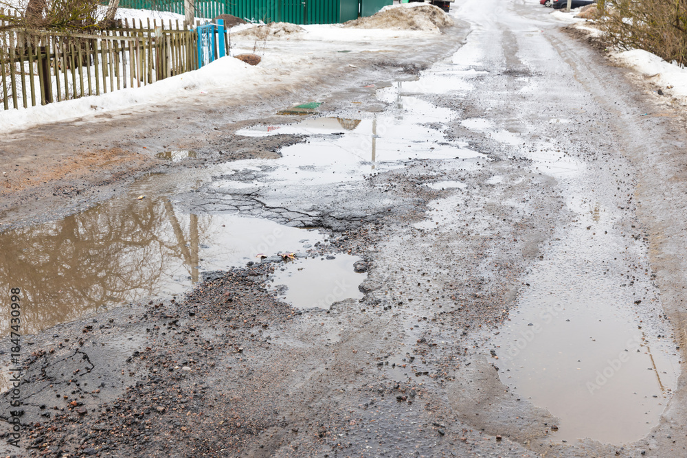 Fototapeta premium A muddy, rain-washed rural street lined with fences and snow piles