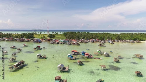 Aerial view of sea gypsy village over clear turquoise waters in Kulapuan Island Semporna, Sabah, Malaysia. Scenic seascape with coral reefs, coastal village, and blue tropical sky.