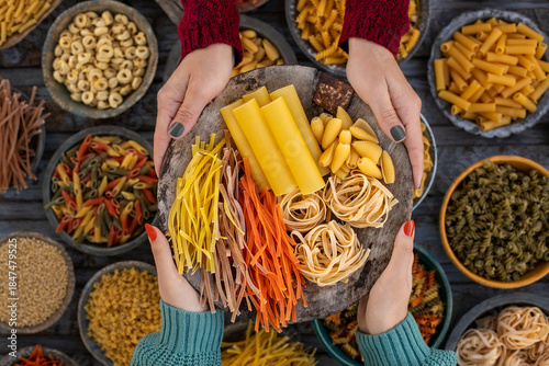 Different types of uncooked pasta at the hands of two women.