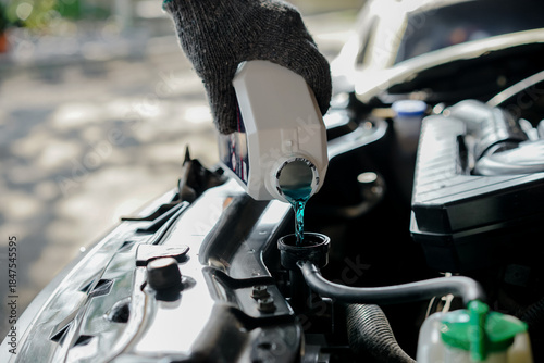  hand is holding a bottle of coolant for refilling the car's radiator, for vehicle maintenance.