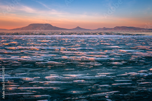 Fonyod, Hungary - Panoramic view of the frozen Lake Balaton on a cold winter afternoon with golden sunset lights and Badacsony mountain at background