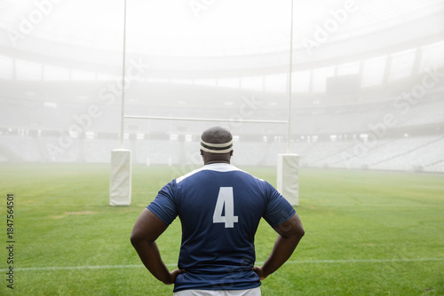 Rugby player is standing on well-kept grass pitch facing rugby goalposts amid light fog