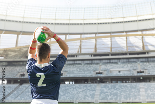 Athlete is standing on grass field holding green and white ball overhead, wearing navy jersey 2