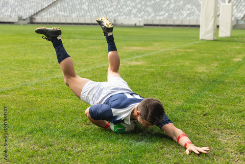 Rugby player is diving forward and is grounding green and white ball on marked grass pitch
