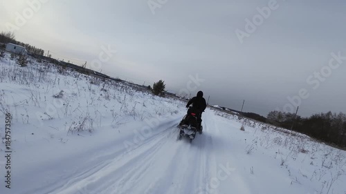 FPV drone following person driving snowmobile on a frozen lake covered with thick snow during the day