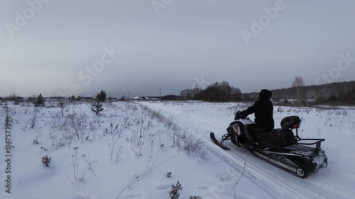 FPV drone following person driving snowmobile on a frozen lake covered with thick snow during the day