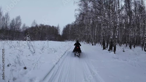 FPV drone following person driving snowmobile on a frozen lake covered with thick snow during the day