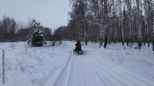 FPV drone following person driving snowmobile on a frozen lake covered with thick snow during the day