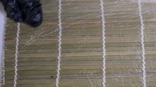 A chef wearing gloves prepares sushi made from rice and various ingredients on a bamboo mat in the kitchen of a Japanese restaurant. Asian cuisine.