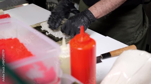 Close-up of chef putting rice on nori in the kitchen of a Japanese restaurant. The process of making sushi in a Japanese restaurant. The chef's hands are gloved.