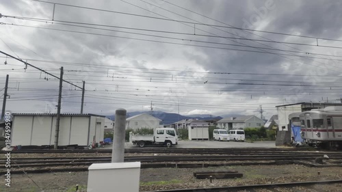 A rural station level crossing with crisscrossing railway tracks and overhead wires, under overcast clouds.