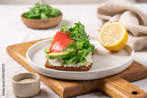 Open sandwich on whole grain bread with smoked salmon, soft cheese, avocado and arugula, healthy gourmet breakfast