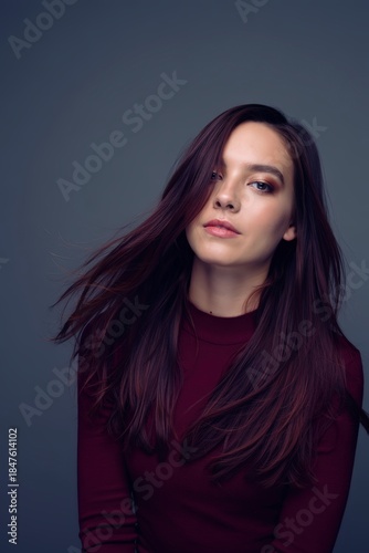 Studio portrait of woman with long flowing burgundy wine colored hair wearing maroon top on gray background, elegant hair color and fashion concept
