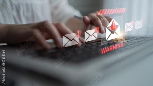 Photos A person typing on a laptop with a visual email warning notification, highlighting the importance of cybersecurity and alertness in digital communication