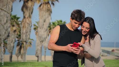 A joyful couple shares a moment as they engage with a smartphone, watching an intriguing video together while smiling and enjoying each other's company in a playful atmosphere.