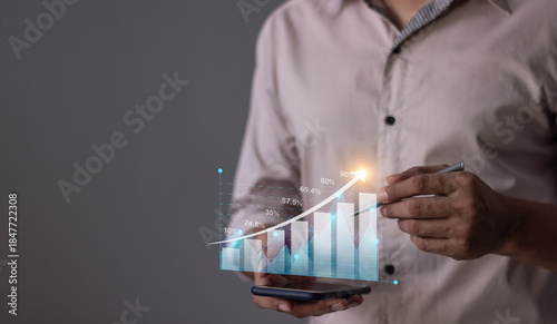 Young man with smartphone hand touching to visualize money growth The phone screen displays graphs and charts showing increasing investment and savings trends, along with an increased account balance