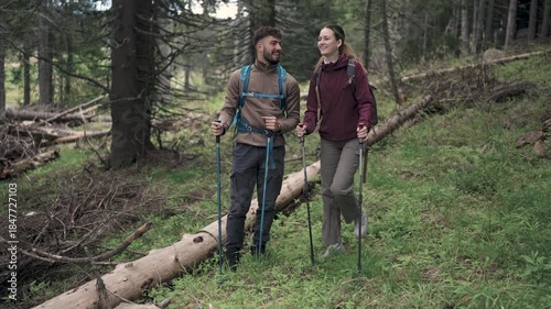 A young couple hiking through a forest with backpacks and walking sticks, enjoying nature and outdoor adventure.