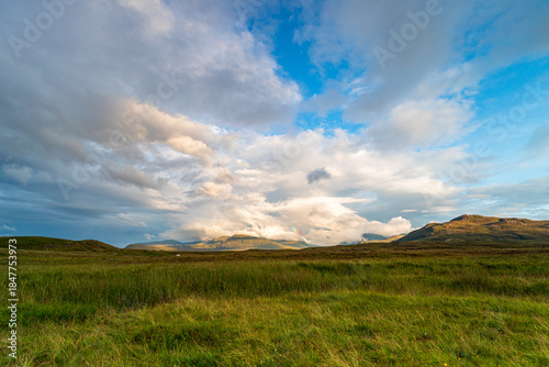 On the NC500, Scotland, open grassland landscape with distant hills under blue sky and dramatic clouds