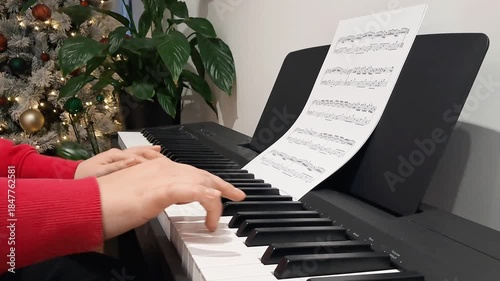 Elegant hands of pianist playing piano near Christmas tree during festive concert