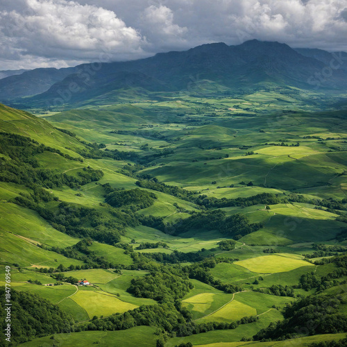 Aerial view of a lush green mountain valley with rolling hills, forests, and a farmhouse under a dramatic cloudy sky.