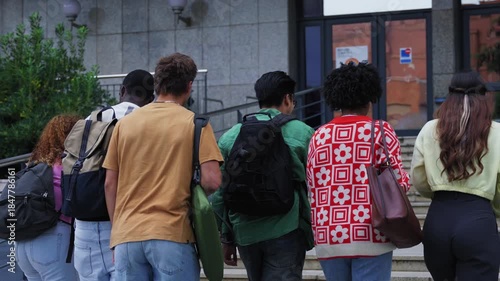 Group of unrecognizable students seen with their backs turned, climbing a flight of stairs to enter the university building. Young academic people on the university campus on their way to class