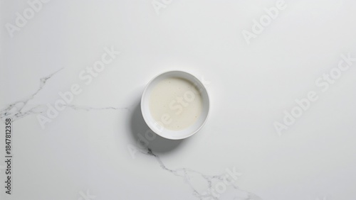 Minimalist flat lay of creamy white liquid in a bowl on Carrara marble background.